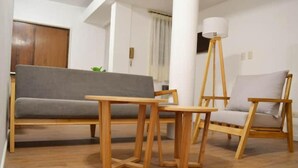 Een woonkamer met een grijze bank, een houten salontafel en stoelen.