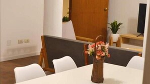 Een vergaderruimte met een witte tafel, houten stoelen, een houten deur en een potplant.