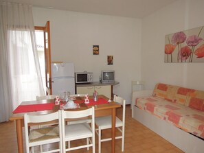 Un espacio habitable compacto con una mesa de comedor, sillas, sofá, kitchenette con microondas, televisor y refrigerador.