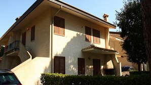A two-story building with a balcony, a car parked in front, and a hedge in the foreground. - Nice flat for 6 guests with private garden (Bibione)