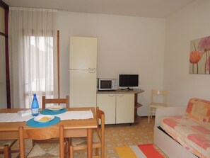 A compact living space with a dining table, chairs, a kitchenette with a microwave, a television, and a sofa. - Villa with garden 250 meters from the beach (Bibione)