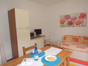 Um quarto pequeno e aconchegante com uma mesa de jantar, um sofá, uma televisão e um armário.