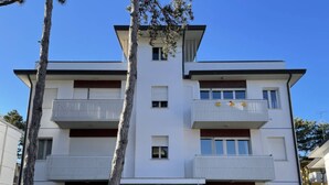 A multi-story residential building with balconies, a central entrance, and a small front garden. - Spacious family apartment for 8 guests (Bibione)