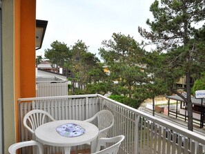 Ein Balkon mit Tisch und Stühlen, einem weißen Geländer und Blick auf Bäume und Gebäude.
