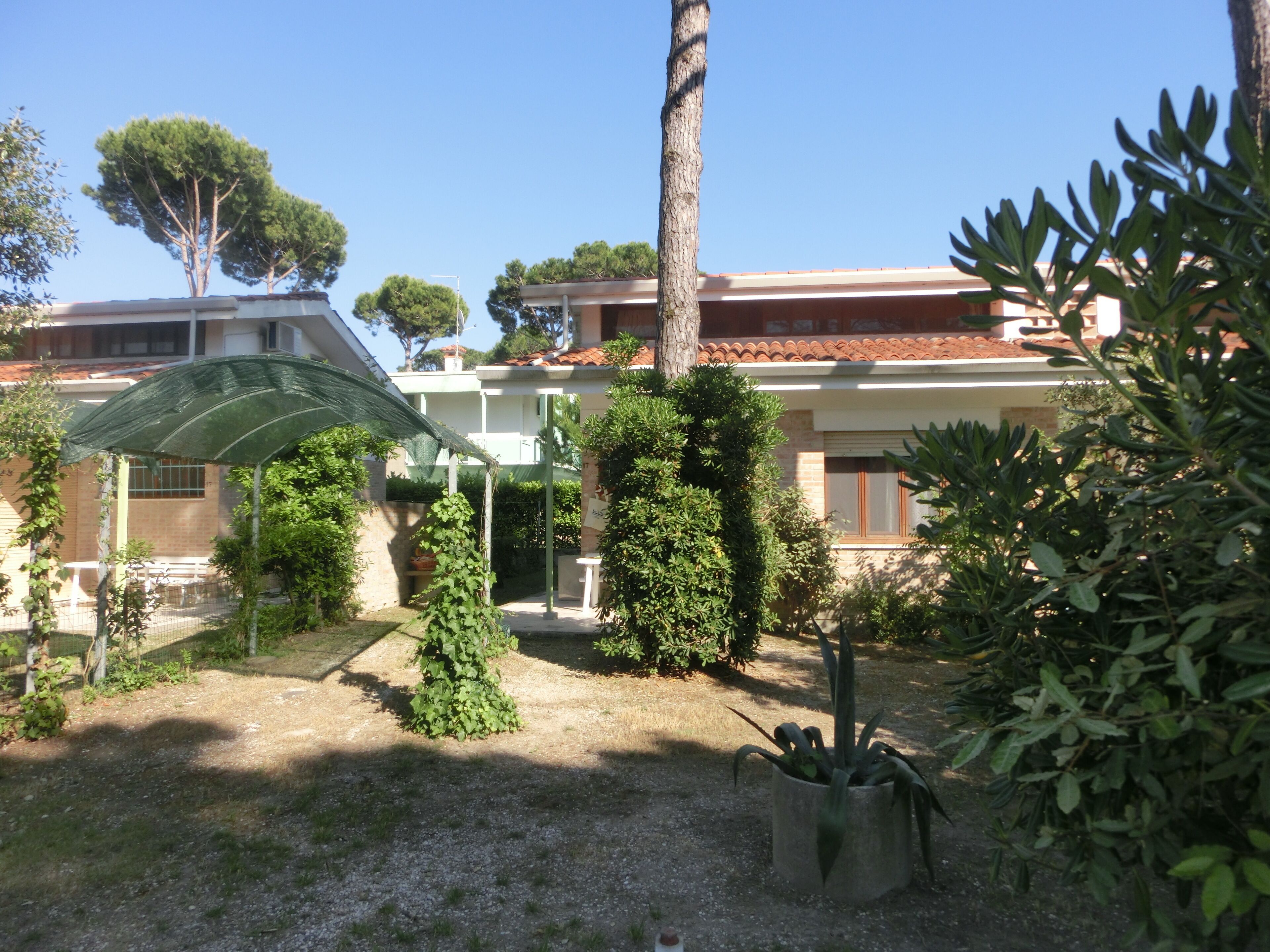 Ein Innenhof mit einer Pergola, Topfpflanzen und einem Gebäude mit einem Ziegeldach.