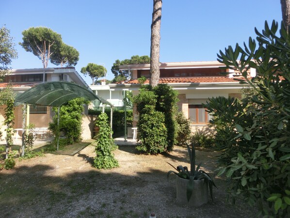 A courtyard with a pergola, potted plants, and a building with a tiled roof.