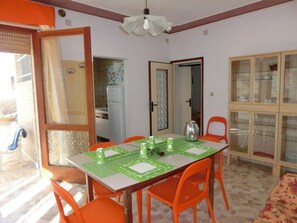 A dining area with a table set for four, surrounded by orange chairs, a cabinet with glass doors, and a doorway leading to another room. - Beautiful flat 250m from the beach for 8 guests (Bibione)