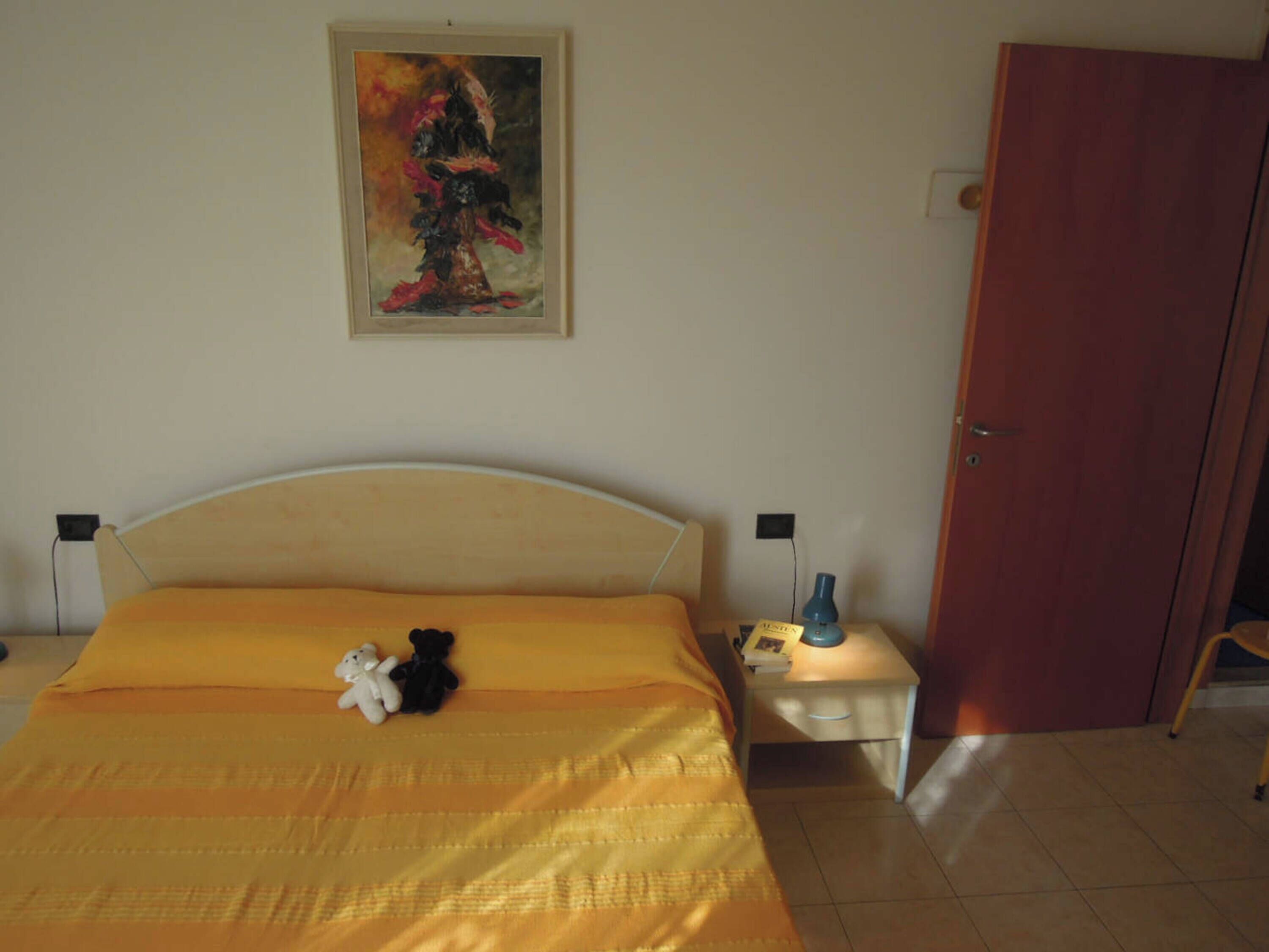 Un dormitorio con cama, dos mesitas de noche, un cuadro y una puerta.