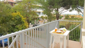 Un balcon avec une table dressée pour le petit-déjeuner, entouré d’une balustrade blanche, donnant sur un quartier résidentiel avec des arbres et une voiture garée.