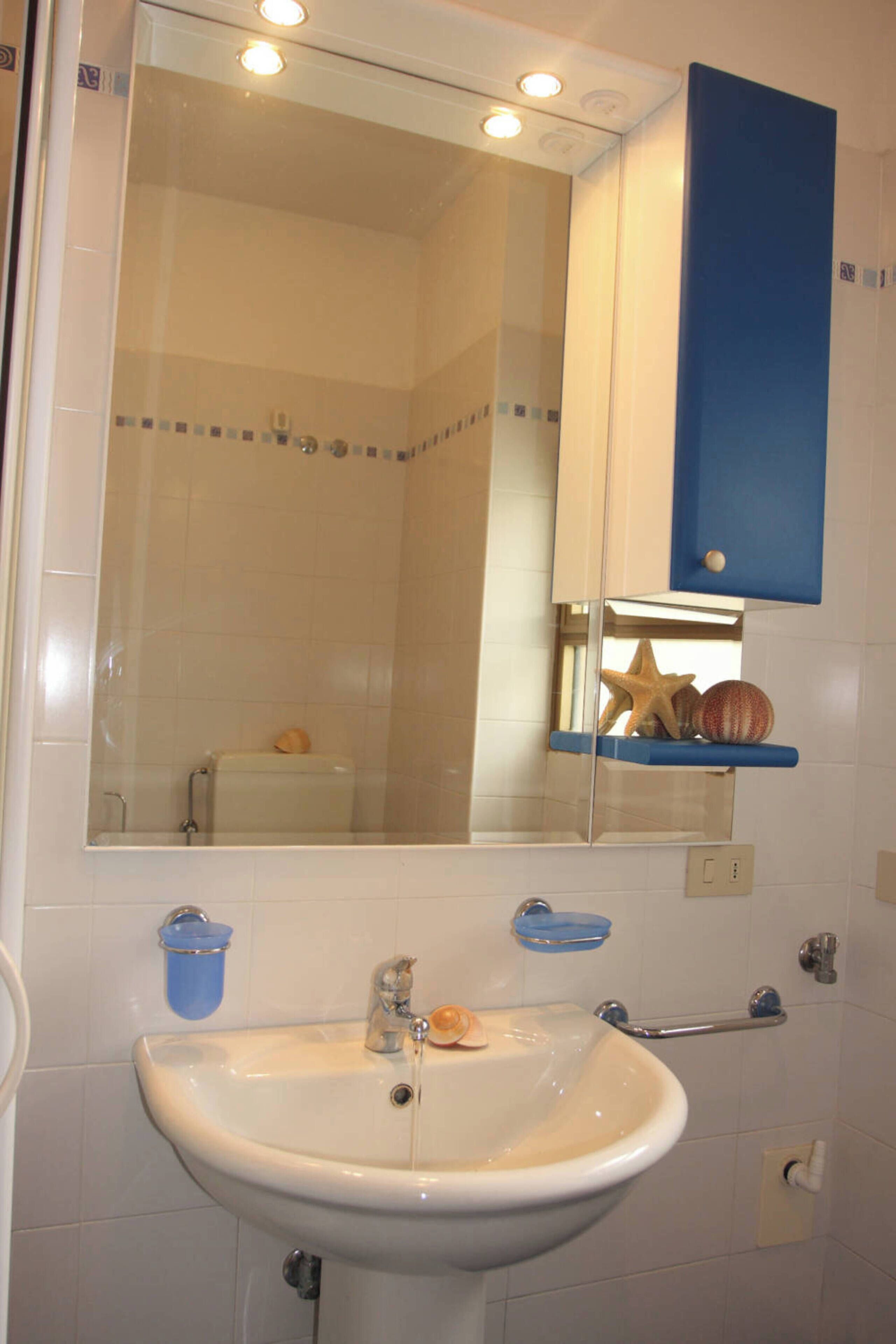 Un baño con lavamanos blanco, un espejo y una estantería azul decorada con objetos.
