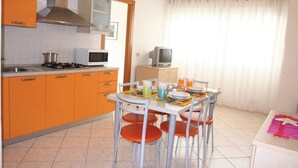 Une cuisine de taille réduite avec des meubles de rangement orange, un four à micro-ondes, une cuisinière et une table à manger avec des chaises.