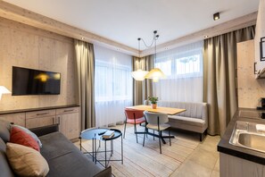 A modern hotel room with a sofa, dining table, chairs, a TV, and a kitchen area. - wohngenuss apprtements (Schladming)