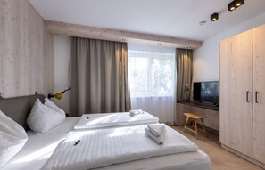 A modern hotel room with two beds, a TV, wooden wardrobe, and a small stool. - wohngenuss apprtements (Schladming)