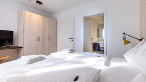 A modern hotel room with a large bed, a TV, wooden wardrobe, and a bathroom visible through an open door. - wohngenuss apprtements (Schladming)