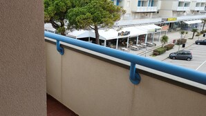 Un balcón con barandilla azul que da a una calle con coches aparcados y un edificio con terraza.