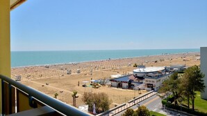 Une vue sur la côte, prise depuis un balcon donnant sur une plage, avec un bâtiment portant l’inscription « Koco » et un ciel dégagé.
