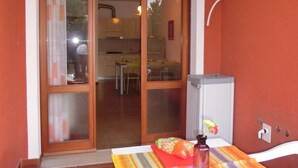 Un coin repas avec une table dressée pour deux personnes, une chaise et une cuisine visible à travers la porte vitrée.