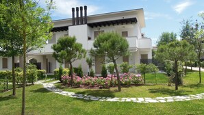 Ein modernes Gebäude mit weißer Fassade, mehreren Schornsteinen und einem Garten mit Bäumen und rosa Blüten.