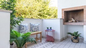 A small patio area with a brick fireplace, a wooden table, two potted plants, and a patterned rug. - Stunning apartment in a holiday village with pool (Bibione)