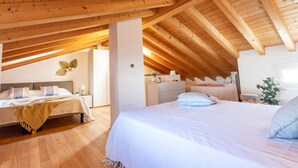 A spacious attic bedroom with wooden beams, two beds, a dresser, and a large window. - Stunning apartment in a holiday village with pool (Bibione)