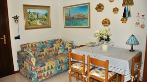 Une pièce comprenant un canapé à motifs, une table à manger avec des chaises, un vase de fleurs et deux tableaux accrochés au mur.