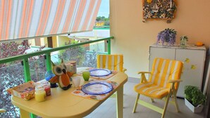 Ein Balkon mit einem gelben Tisch, gedeckt für zwei Personen, gestreifte Stühle und einem dekorativen Wandelement.
