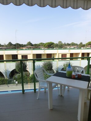 A covered outdoor area with a table and chairs, a pool, and a building in the background. - Family-friendly poolside tranquility (Bibione)