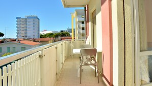 Ein Balkon mit Tisch und Stühlen, einem weißen Geländer und Blick auf Gebäude im Hintergrund.