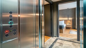 An elevator with control buttons and a view into a modern bedroom with a bed and bedside table. - Urban Quarters - Gülhane (Istanbul)