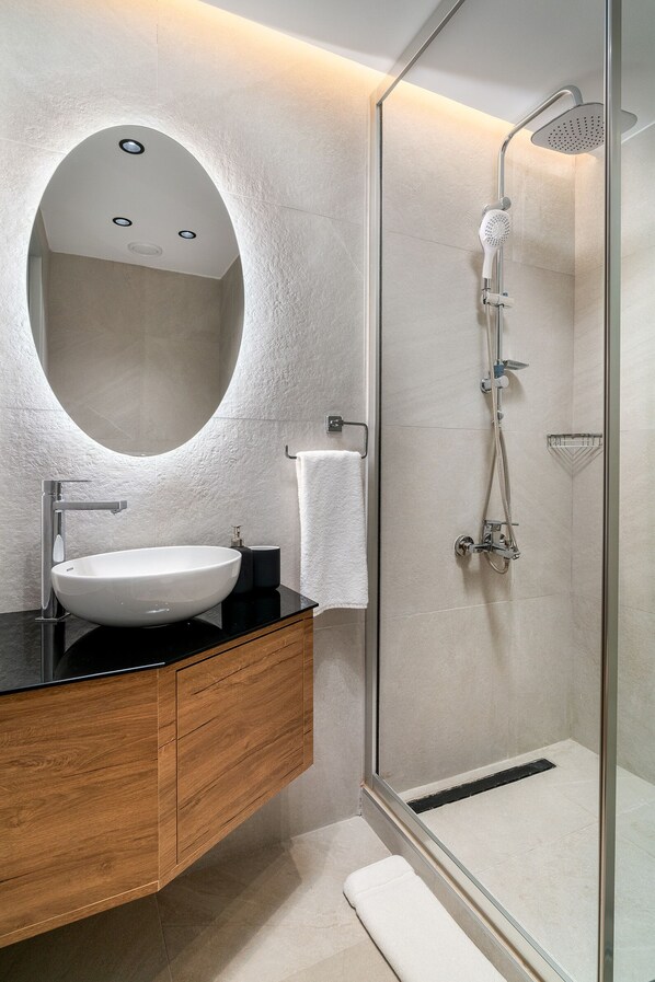 Un baño moderno con un espejo redondo, un lavabo blanco y una ducha con cerramiento de vidrio.