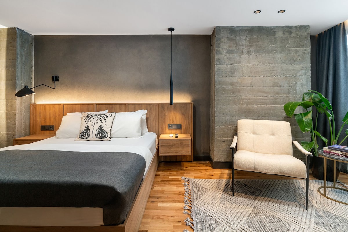 A modern bedroom with a wooden bed, a nightstand, a chair, and a large plant.