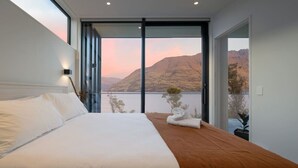 Quarto de hotel moderno com uma cama grande, vista para montanhas e varanda.
