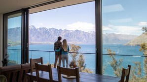 A couple standing by a large window overlooking a lake and mountains. - Crystal Waters- Suite 4 (Queenstown)