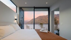 A modern hotel room with a large bed, a view of mountains, and a balcony with a plant. - Crystal Waters- Suite 4 (Queenstown)