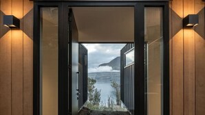 A modern building entrance with a wooden facade, glass doors, and a view of a body of water and mountains.