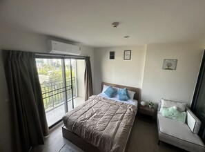 A hotel room with a large bed, a bedside table, a chair, a window with curtains, and a wall-mounted air conditioner. - La casita Hua Hin (Hua Hin)