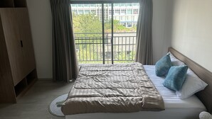 A bedroom with a bed, a wardrobe, an air conditioning unit, and a balcony with a view of buildings and greenery. - La casita Hua Hin (Hua Hin)