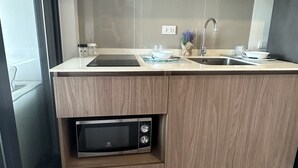 A modern kitchen with wooden cabinetry, a built-in microwave, a stainless steel sink, and a range hood. - La casita Hua Hin (Hua Hin)