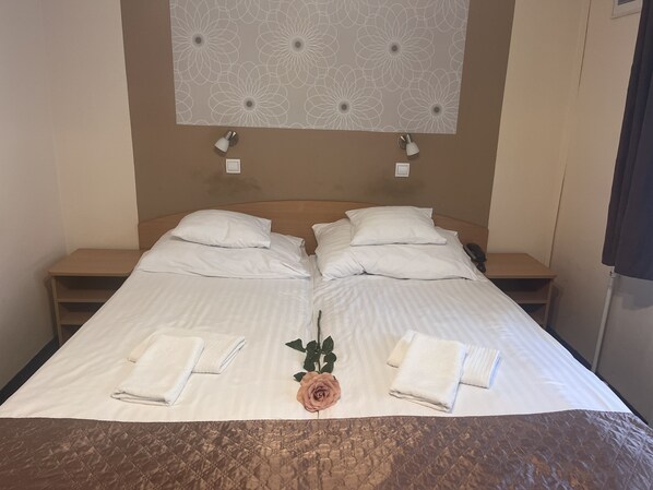 A double bed with white linens, two bedside tables, a decorative wall panel, and a single potted plant. - Hotel Rose City (Budapest)
