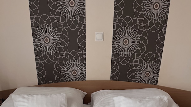 A double bed with white linens, two pillows, a rose, and folded towels. - Hotel Rose City  (Budapest)