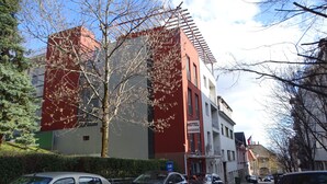 A hotel building with a red and white facade, parked cars along the street, and leafless trees. - Hotel Rose City  (Budapest)