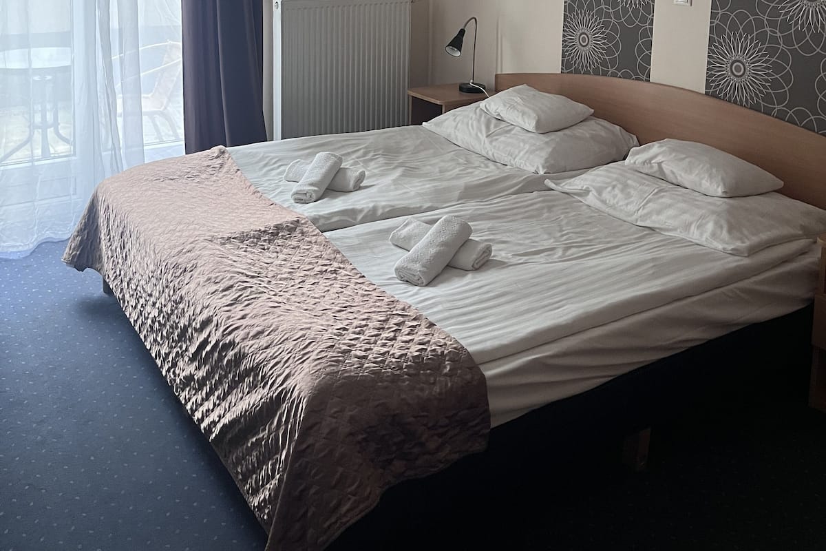 A hotel room with a large bed, a bedside lamp, a radiator, and a window with curtains.