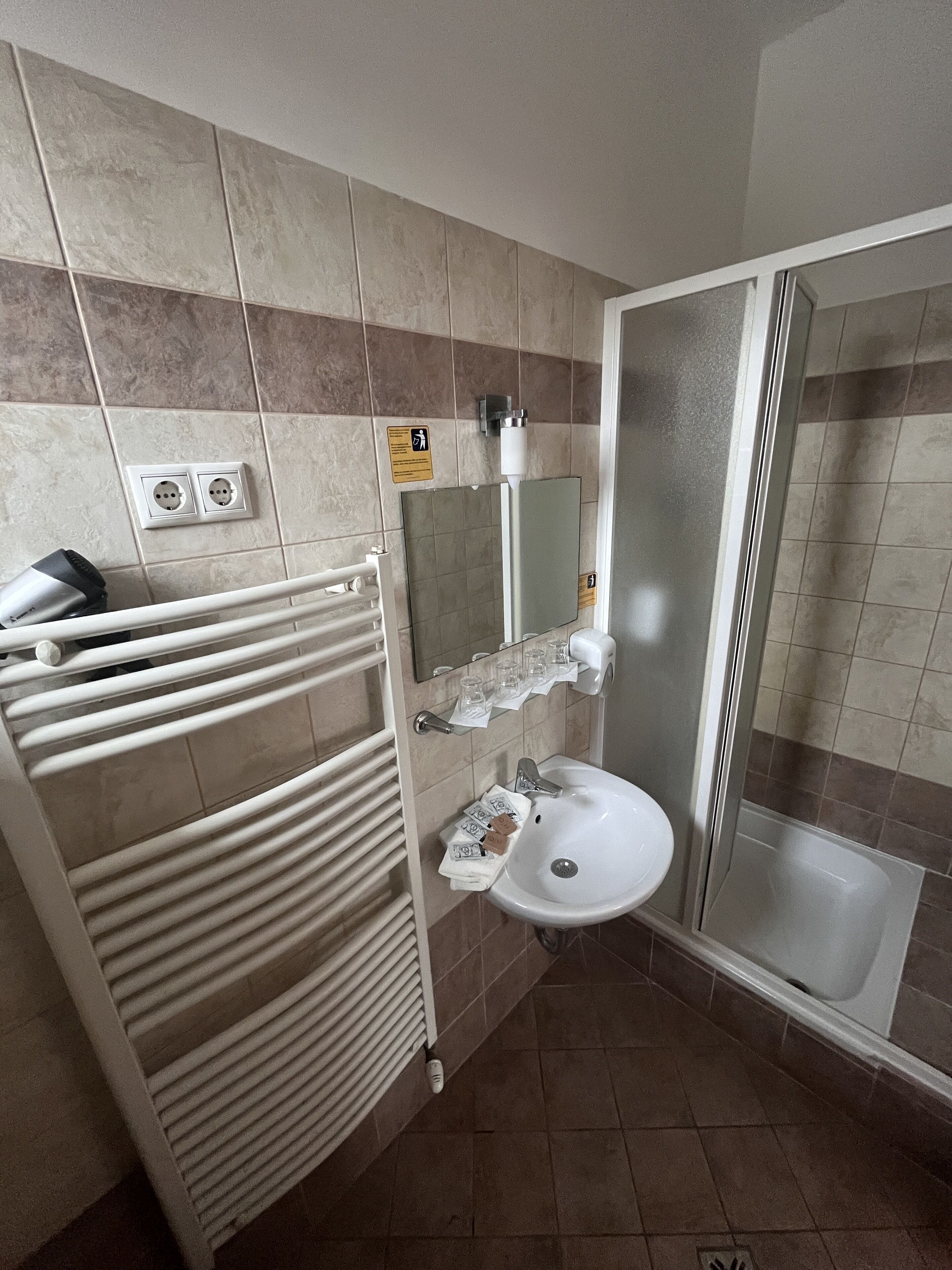 Een badkamer met een witte wastafel, spiegel en douchecabine. Handdoekhouder en plank met toiletartikelen.