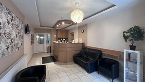 A hotel lobby with a reception desk, a black leather sofa, a black trash bin, a potted plant, and a television on the wall. - Hotel Rose City  (Budapest)