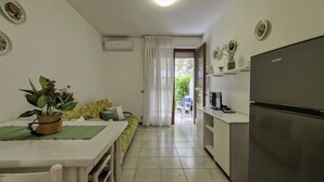 A compact kitchen with a refrigerator, a dining table with a plant, and a sofa with a colorful cushion. - Spacious flat surrounded by nature - Beahost (Bibione)
