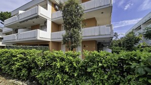 A multi-story residential building with balconies, a central tree, and a well-maintained hedge in front. - Spacious flat surrounded by nature - Beahost (Bibione)