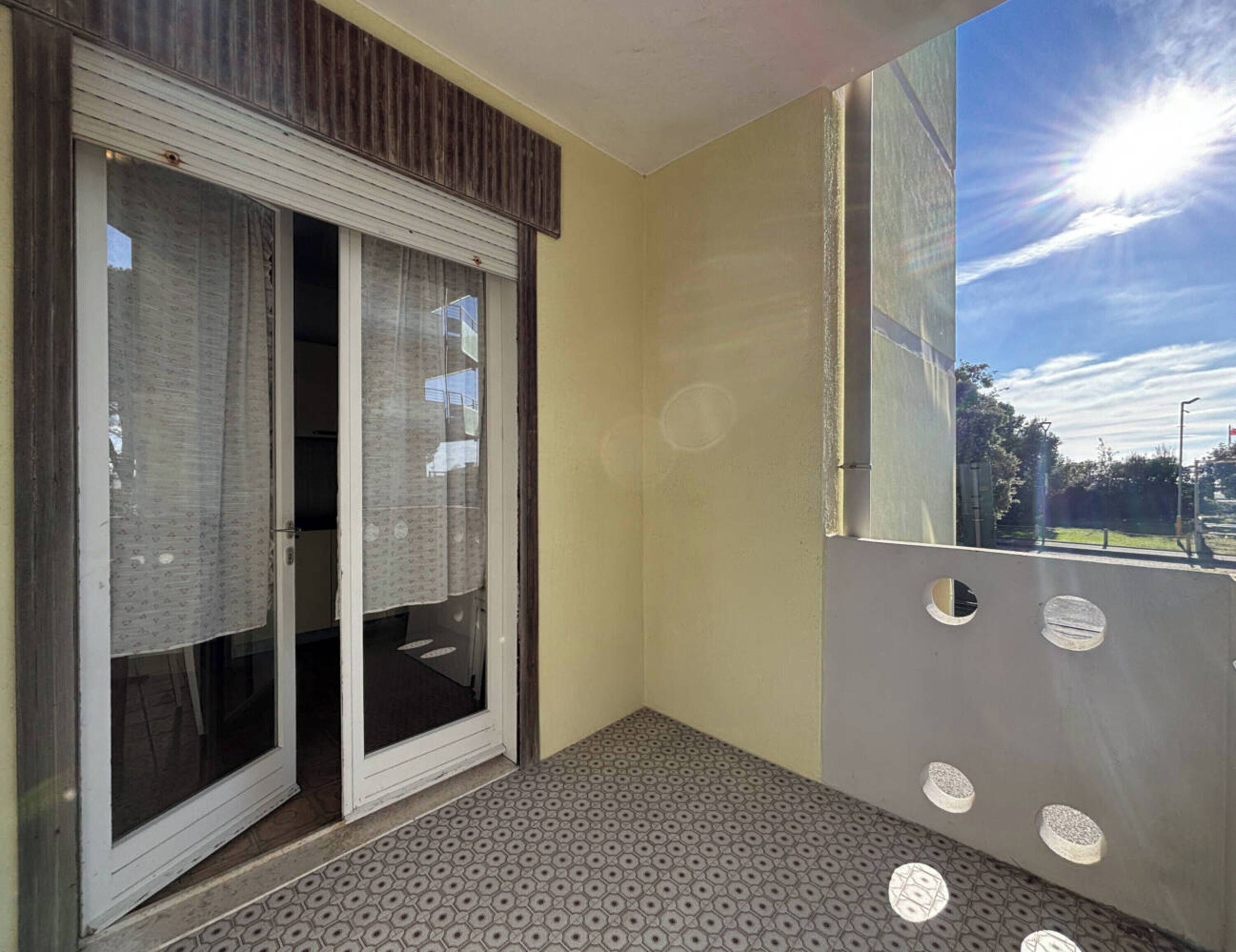 Uma varanda com piso estampado, porta de correr de vidro e vista para o céu e árvores.