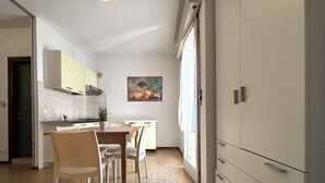 A compact kitchen with a dining area, a painting on the wall, and a large window. - Nice studio with side sea view (Bibione)