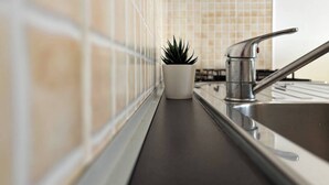 A kitchen with a stainless steel sink, a potted plant, and tiled backsplash. - Nice studio with side sea view (Bibione)