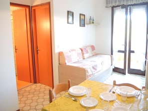 Una stanza con un tavolo da pranzo apparecchiato per quattro persone, un divano con rivestimento decorato e una porta vetrata scorrevole che dà su uno spazio esterno.